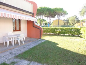 A patio with a table and chairs, a small garden, and a building with a curved facade. - Ground-floor flat with garden (Bibione)