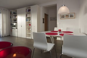 A modern living room with a dining area, white furniture, and a bookshelf. - Holiday apartment in Norderney with Wi-Fi (Norderney)