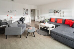 A modern living room with a grey sofa, a coffee table, and a dining area with a white table and chairs. - Holiday apartment in Norderney with Wi-Fi (Norderney)