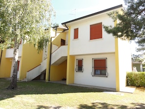 Um edifício de vários andares com escadaria, uma árvore e um gramado bem cuidado.