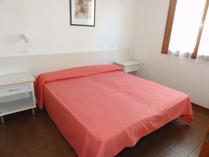 Quarto com cama, mesa de cabeceira, gaveta, quadro na parede e janela com cortinas.