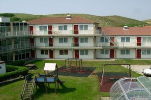 Ein mehrstöckiges Gebäude mit rotem Ziegeldach, Balkonen und einem Spielplatz mit Spielgeräten.