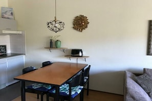 A compact kitchen with a dining area, a coffee maker on a shelf, and a wall-mounted decorative item. - Beach Apartment 38 "Dune View" (GH Callantsoog)