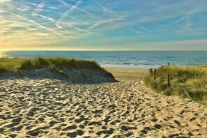 A sandy beach with footprints leading to the water, a clear sky, and a person in the distance. - Beach Apartment 38 "Dune View" (GH Callantsoog)