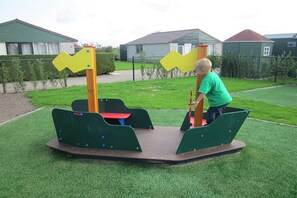 A child playing on a playground with a seesaw and a swing set. - Holiday home with 1 bedroom (Burgerbrug)