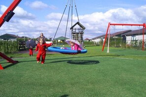 A playground with a swing set, a climbing structure, and a fenced area. - Holiday home with 1 bedroom (Burgerbrug)