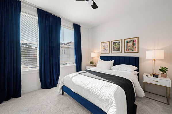 Un dormitorio con una cama, dos mesitas de noche, un aparador, una ventana con cortinas y decoración en la pared.