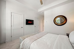 Quarto com uma cama, uma televisão na parede e um espelho redondo.