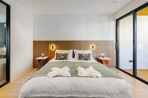 Quarto de hotel moderno com uma cama grande, duas mesas de cabeceira e uma janela ampla.