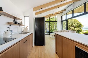 Une cuisine moderne avec des meubles en bois, un réfrigérateur noir et une grande fenêtre donnant sur un paysage verdoyant.