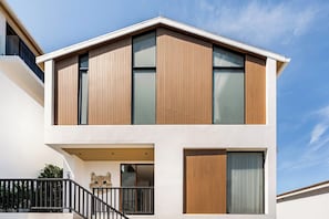 A modern two-story building with a flat roof, large windows, and a balcony with a black railing.