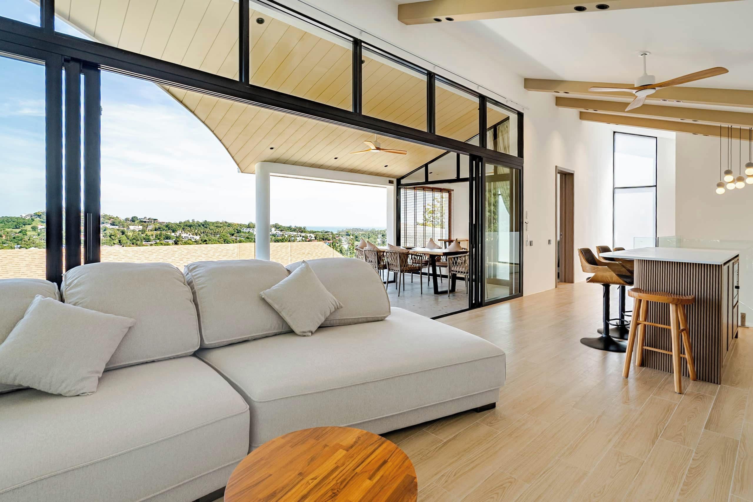 A modern living room with a large sofa, wooden coffee table, and a dining area with chairs and a table.