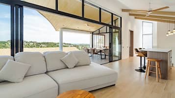 A modern living room with a large sofa, wooden coffee table, and a dining area with chairs and a table.