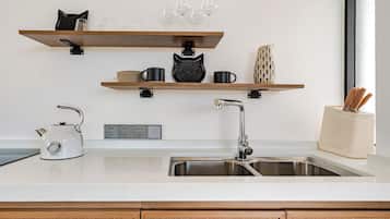 Een keuken met een wit aanrecht, een roestvrijstalen spoelbak, een waterkoker en houten planken met mokken en glazen.