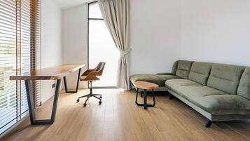 A modern living room with a wooden floor, a green sofa, a wooden coffee table, and a desk with a chair.