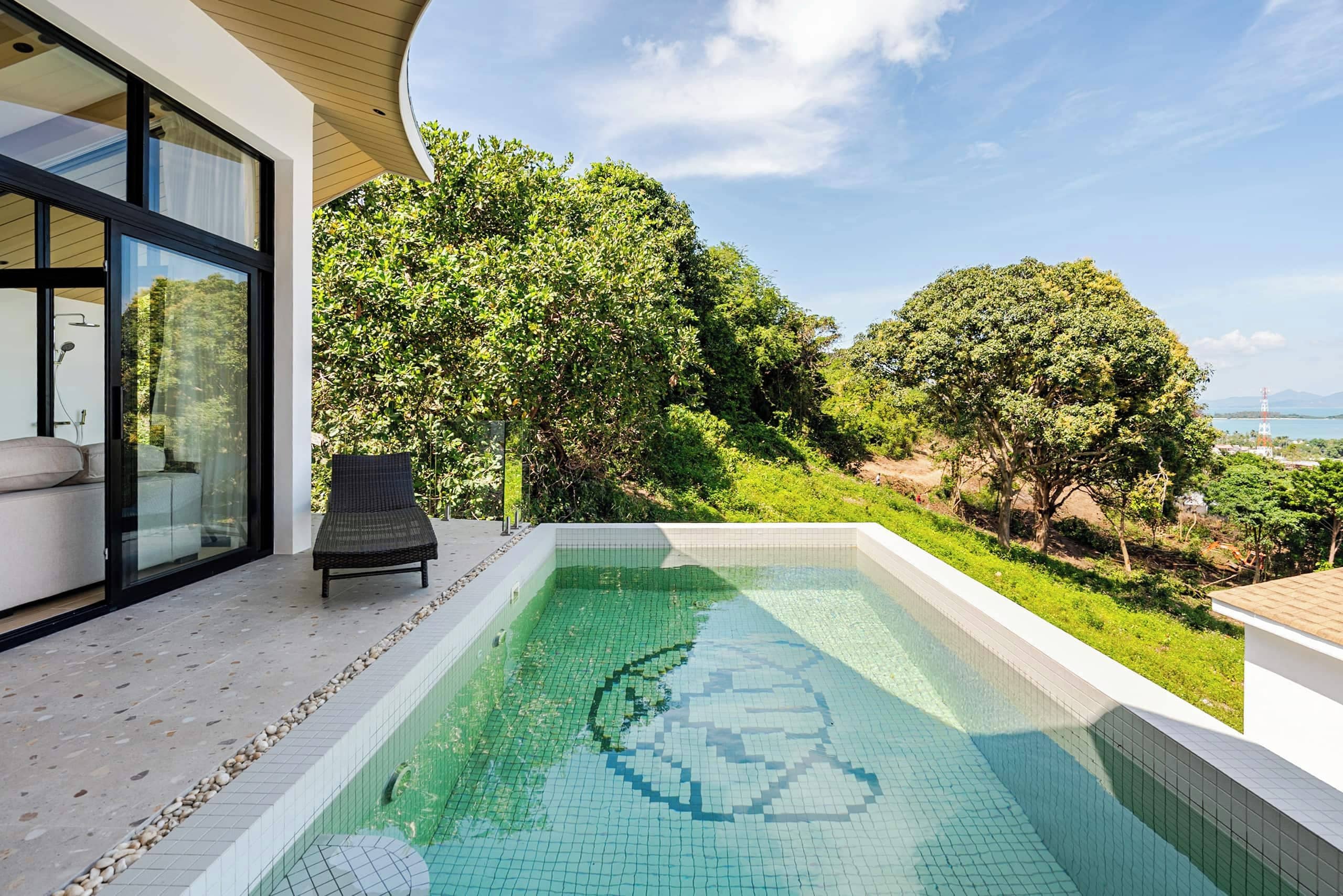 A modern outdoor swimming pool with a clear view of the surrounding greenery and a distant landscape.