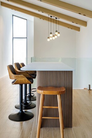 Uma área de bar moderna com uma ilha central, banquetas e iluminação pendente.