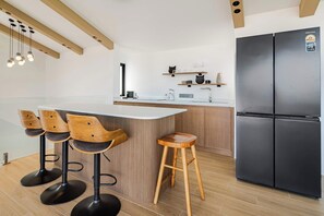 Une cuisine moderne dotée d’un îlot central, de tabourets de bar, d’un réfrigérateur noir et de meubles de rangement en bois.
