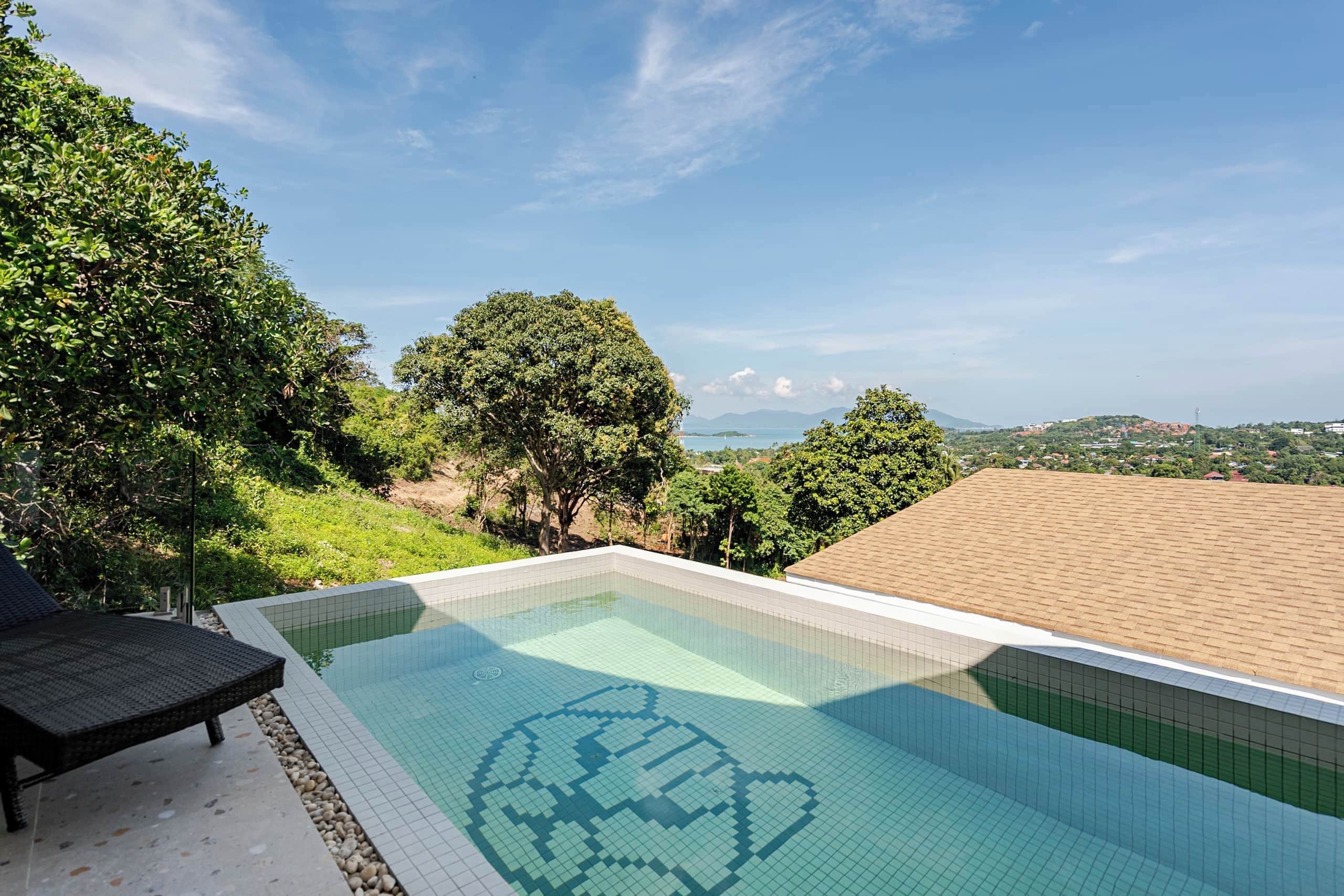 Piscina com design de azulejos em formato de coração, rodeada por vegetação exuberante e céu claro.