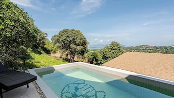 Piscina com design de azulejos em formato de coração, rodeada por vegetação exuberante e céu claro.