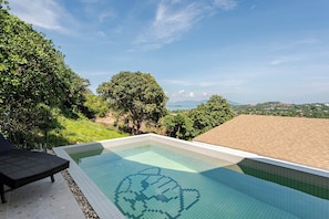 A swimming pool with a heart-shaped tile design, surrounded by lush greenery and a clear sky.