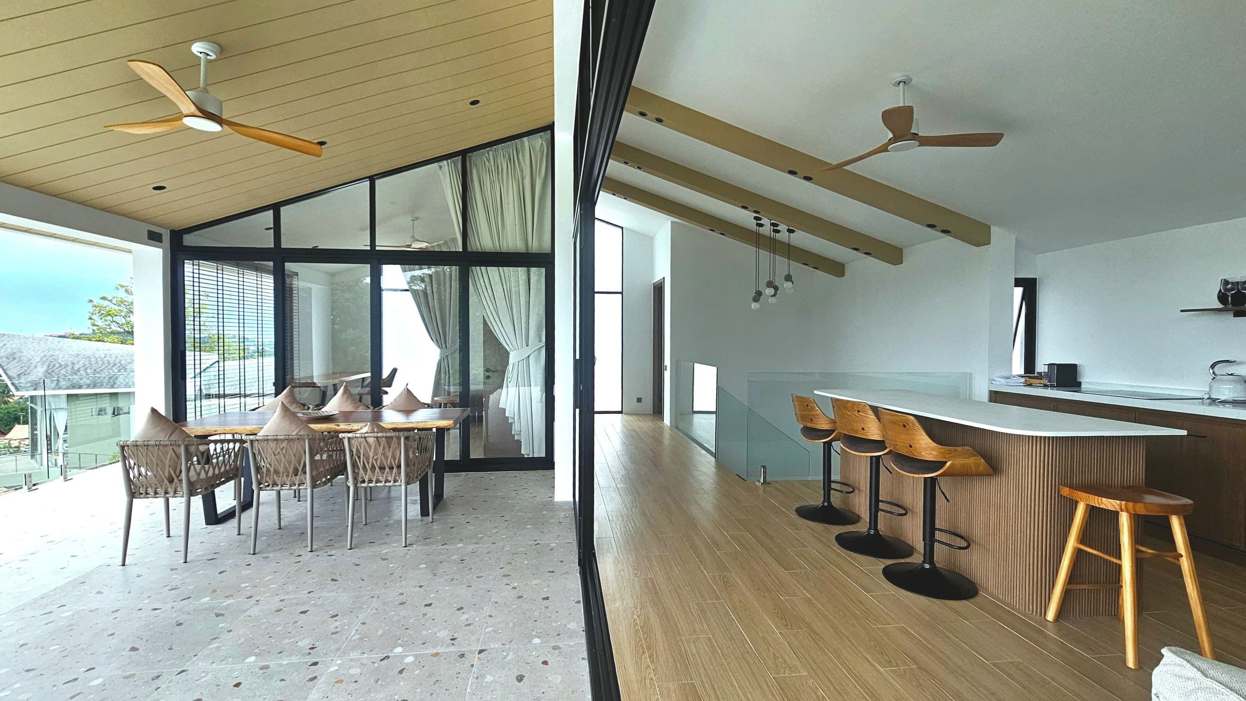 Una cocina moderna con taburetes de madera, una zona de comedor con sillas y ventanas amplias.