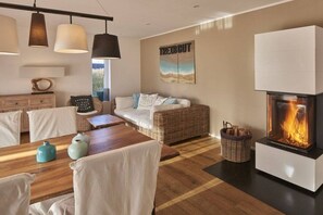 A modern living room with a fireplace, a sofa, a dining table, and hanging pendant lights. - Strandhaus Treibgut new in 2015 (Großenbrode)