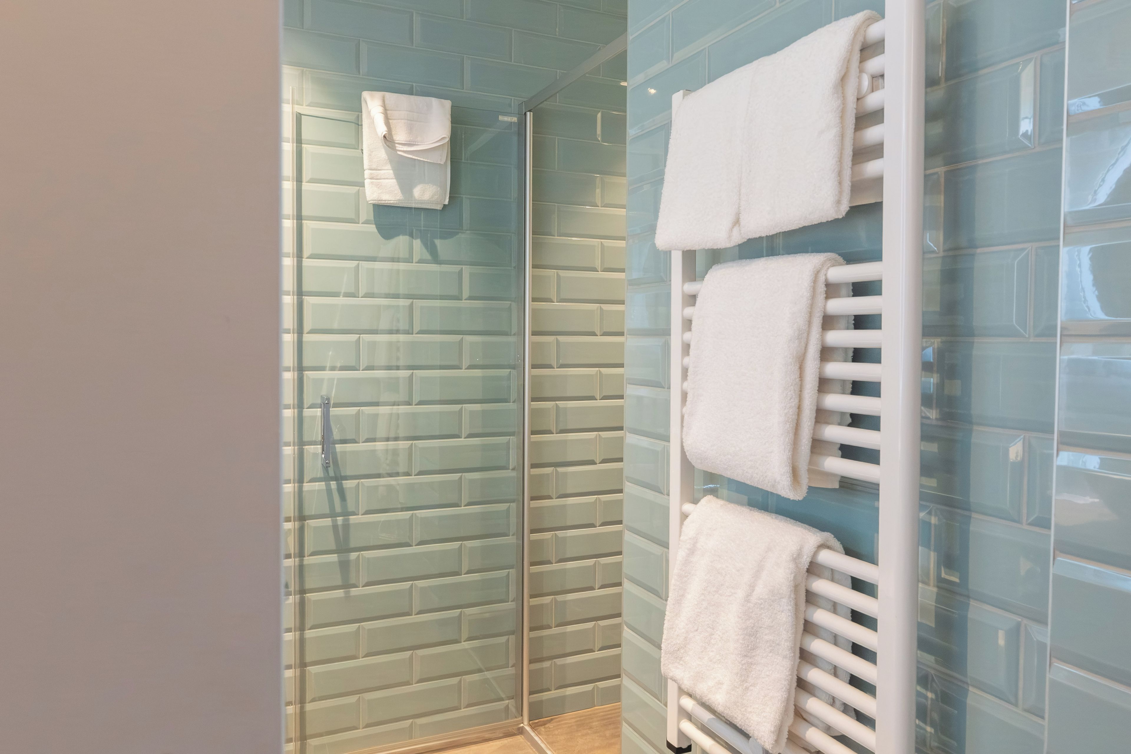 A bathroom with a glass shower enclosure, a white towel rack, and a tiled wall.
