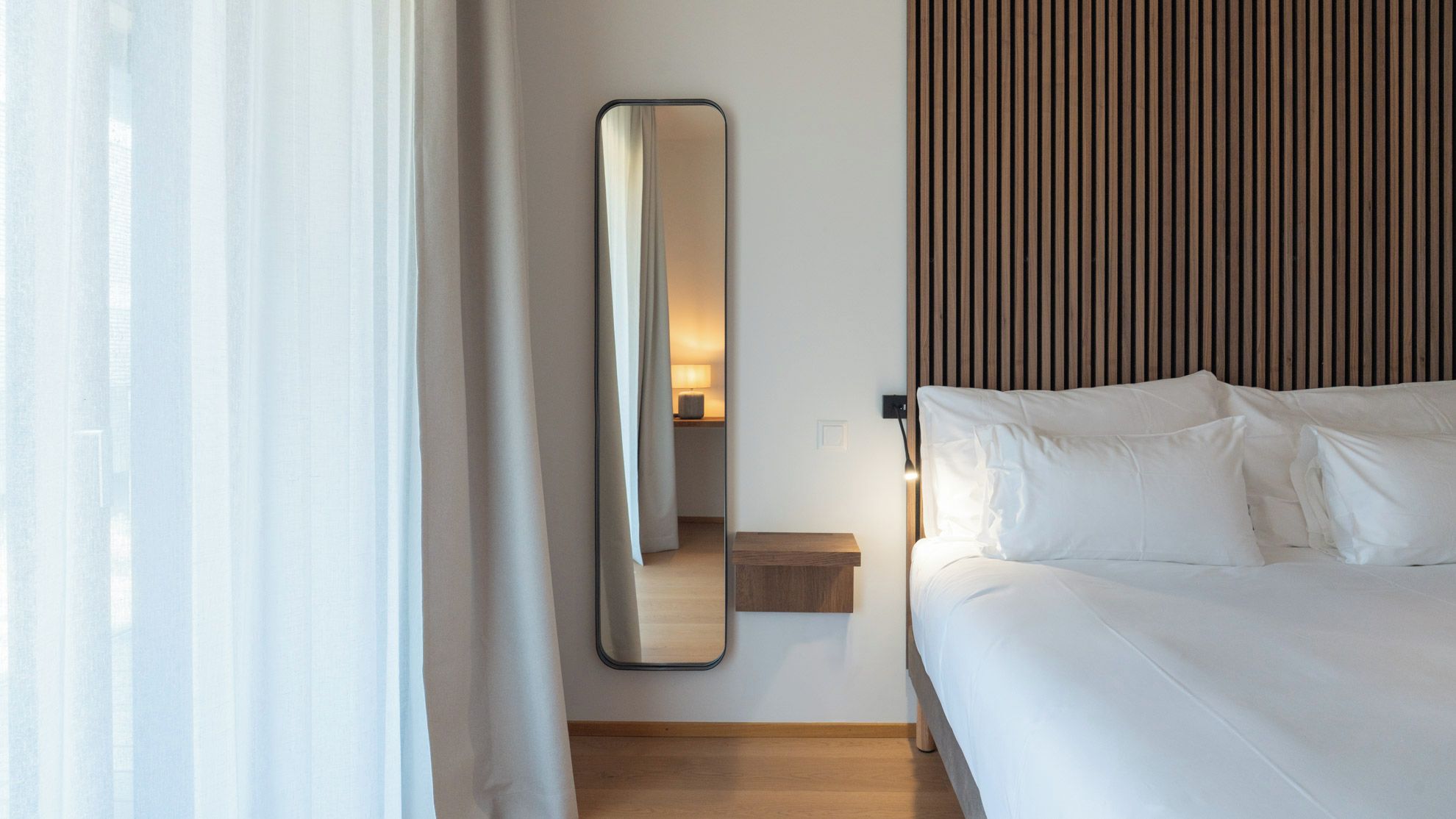Una camera d'albergo con un letto, un comodino, uno specchio e una parete rivestita in legno.