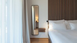 A hotel room with a bed, a bedside table, a mirror, and a wooden panel wall.