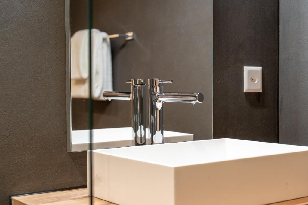 A modern bathroom with a white sink, chrome faucet, and a mirror reflecting a towel.