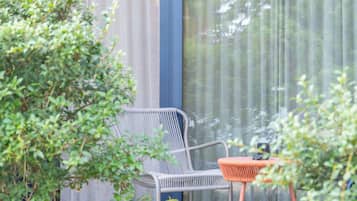 Una silla de mimbre y una mesita con cojín, ubicadas frente a una ventana con cortina estampada.