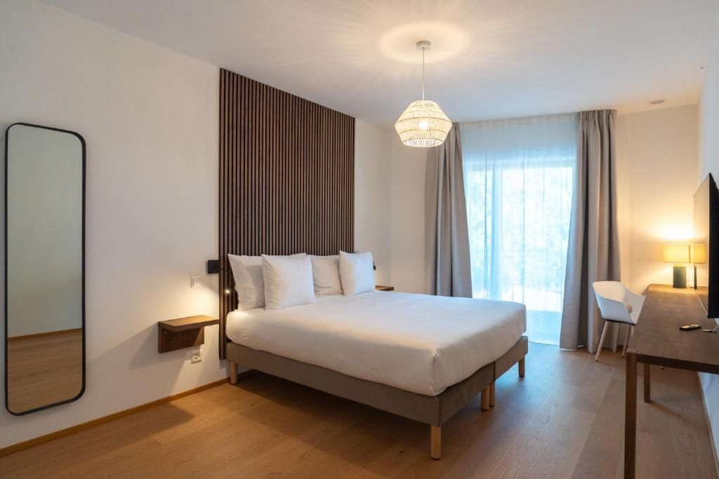 A hotel room with a bed, bedside table, lamp, chair, and a large mirror.