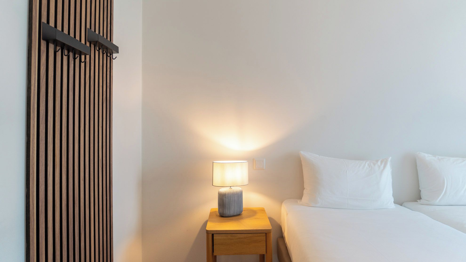 Una habitación de hotel con una cama, una mesita de noche con lámpara y un panel de madera en la pared.