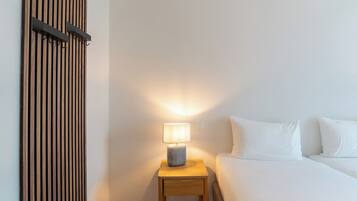 Una habitación de hotel con una cama, una mesita de noche con lámpara y un panel de madera en la pared.