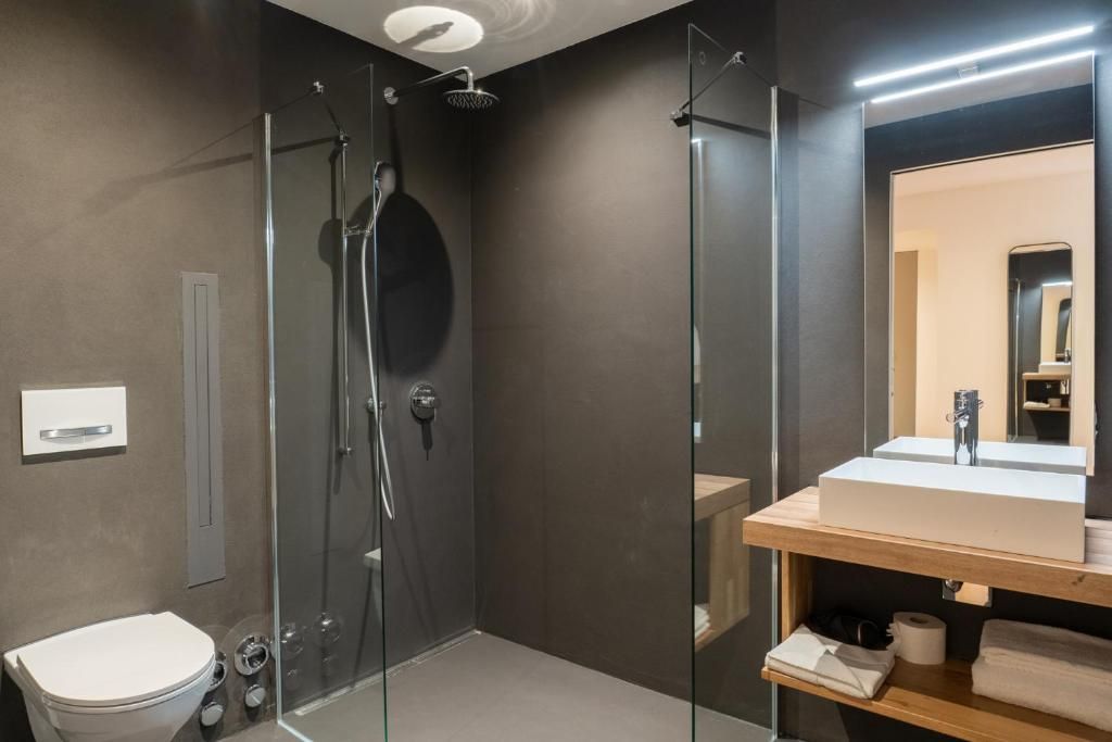A modern bathroom with a glass-enclosed shower, a white toilet, and a wooden vanity with a mirror.