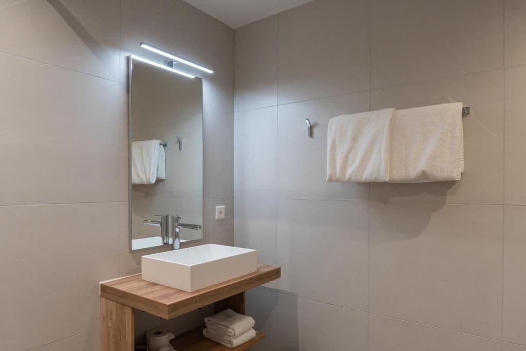 Un baño moderno con un lavamanos rectangular, un espejo y dos toallas en un perchero.