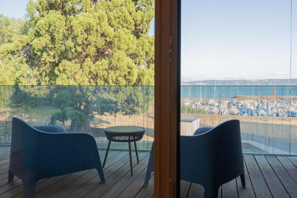A balcony with two chairs and a small table, overlooking a coastal area with trees and a view of the sea.