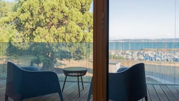 A balcony with two chairs and a small table, overlooking a coastal area with trees and a view of the sea.
