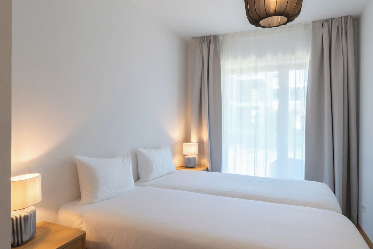 A hotel room with a large bed, a bedside table with a lamp, and a window with curtains.