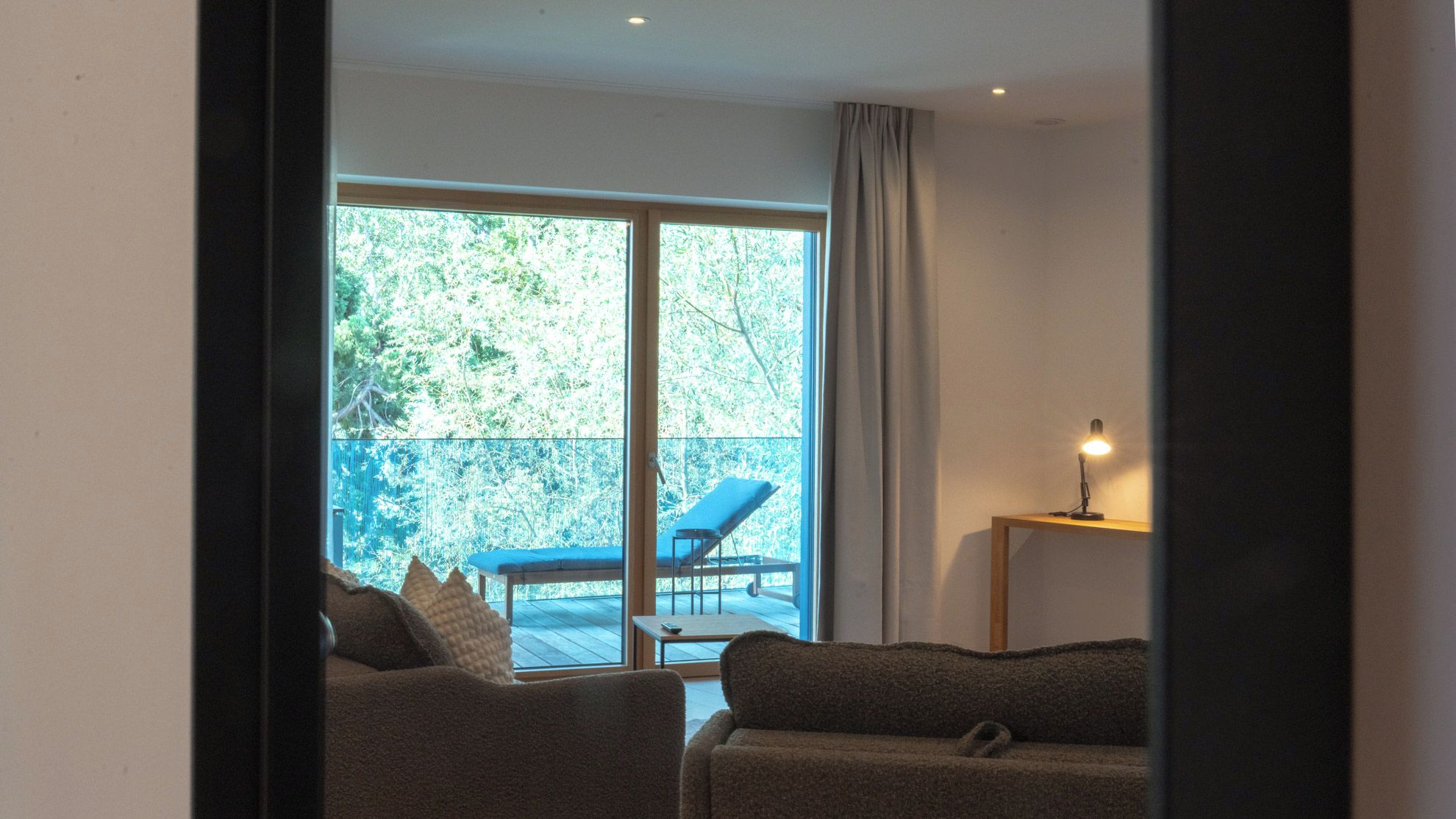 Una habitación con un sofá, una mesita de noche con una lámpara y vistas a un balcón con una silla.