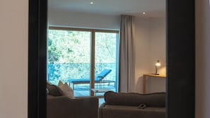 A room with a sofa, a small table with a lamp, and a view of a balcony with a chair. - Pattùs Hôtel (LA GRANDE BÉROCHE)