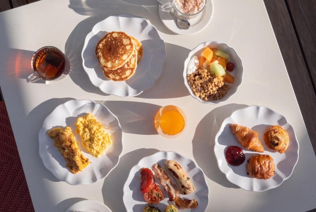 Mesa de café da manhã com vários pratos, incluindo panquecas, ovos mexidos, croissants e frutas.