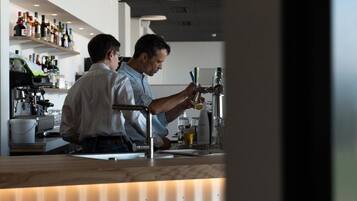 Zona de bar con mostrador, estanterías llenas de botellas y una persona sirviendo una bebida.