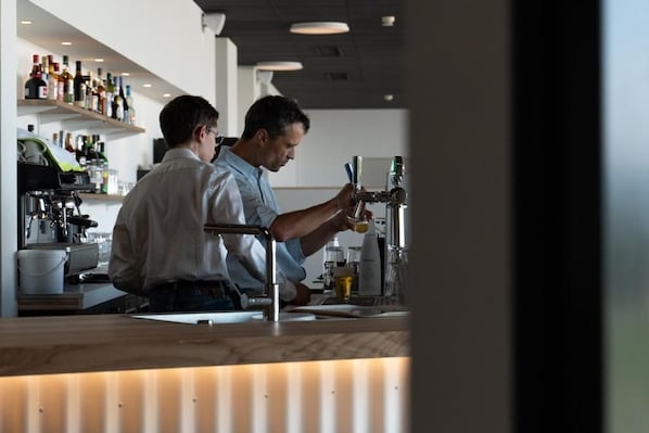 Zona de bar con mostrador, estanterías llenas de botellas y una persona sirviendo una bebida.
