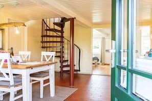 A dining area with a wooden table and chairs, a spiral staircase, and a view through a green-framed window. - Holiday home with 2 bedrooms (Langballig)