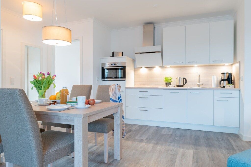 Une cuisine moderne avec des meubles blancs, un four encastré et un coin repas comprenant une table et des chaises.