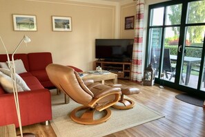 A living room with a red sofa, a leather recliner, a television, and a large window with curtains. - with a view of the Bodden (Groß Zicker)