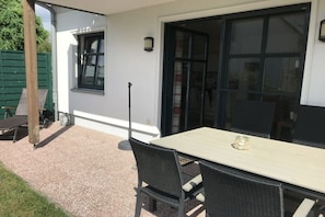 Eine Terrasse im Freien mit Tisch und Stühlen, einem grünen Zaun und einem Fenster.