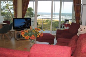 Ein Wohnzimmer mit Fernseher, roten Möbeln, einer Blumenvase und Blick auf den Ozean.